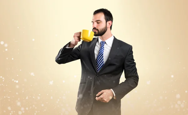 Joven hombre de negocios bebiendo un café sobre fondo ocre —  Fotos de Stock