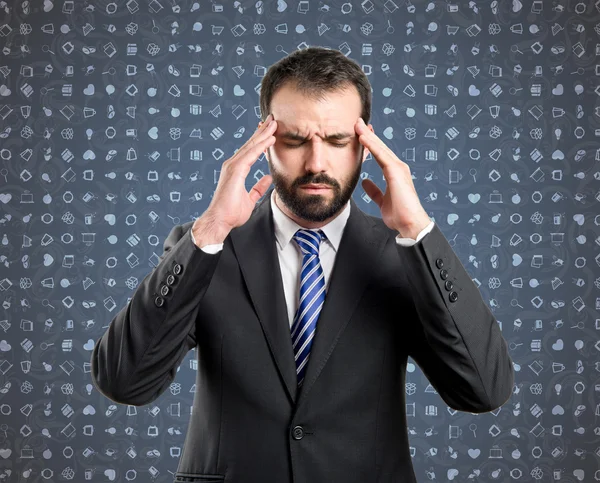 Joven hombre de negocios con dolor de cabeza sobre fondo azul con iconos — Foto de Stock