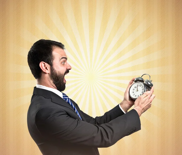 Joven hombre de negocios sosteniendo un reloj antiguo sobre fondo ocre — Foto de Stock