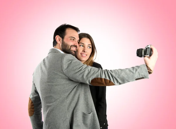 Homem fotografando com sua namorada sobre fundo rosa — Fotografia de Stock