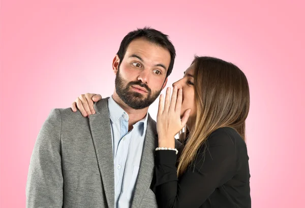 Jong meisje aan haar vriendje fluisteren over roze achtergrond — Stockfoto