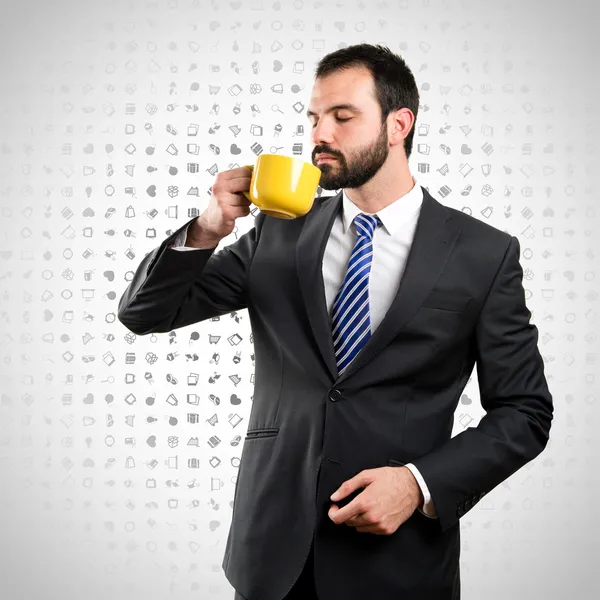 Ung affärsman dricka en kopp kaffe över bakgrund med ikoner — Stockfoto