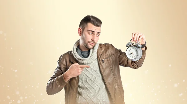 Young businessman holding an antique clock over ocher background — Stock Photo, Image
