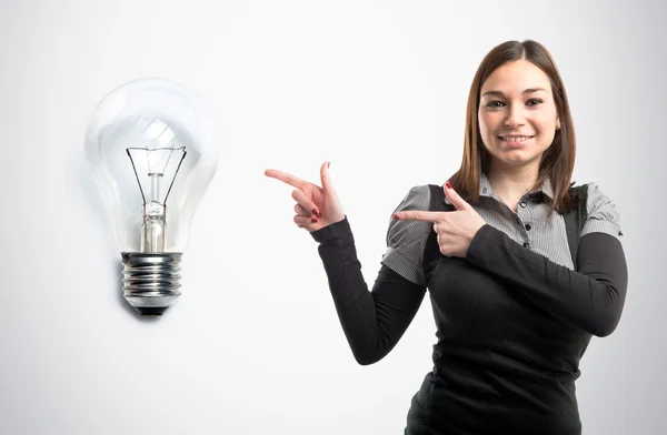 Jonge mooie woman wijzend een gloeilamp over grijze achtergrond — Stockfoto