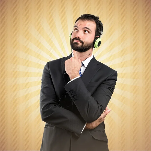 Joven hombre de negocios escuchando música sobre fondo ocre — Foto de Stock