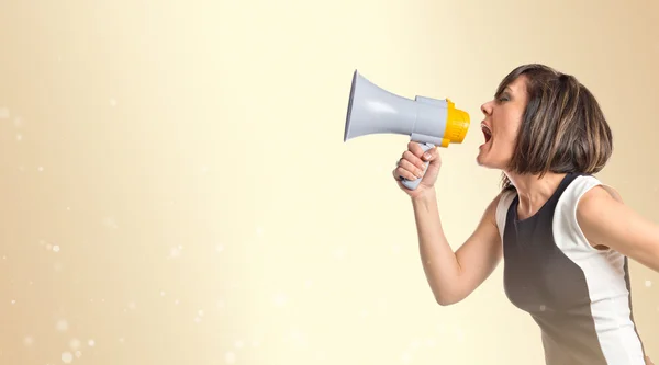 Pretty girl shouting with a megaphone over ocher background — Stock Photo, Image