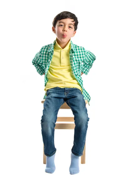 Menino fazendo uma zombaria na cadeira de madeira sobre branco — Fotografia de Stock
