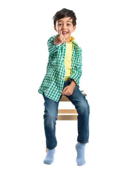 Мальчик указывает на фронт на деревянном стуле на белом фоне — стоковое фото