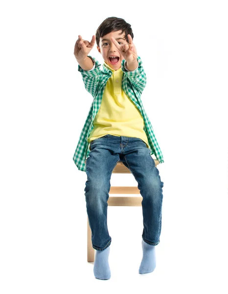 Niño haciendo el cartel del cuerno en la silla de madera — Foto de Stock