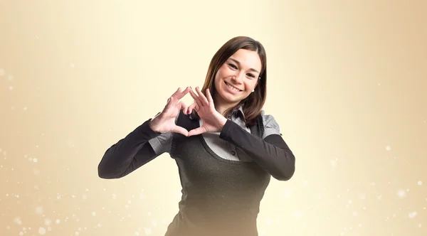 Genç kadın yapım kalp hareketi koyu sarı bir arka plan üzerinde — Stok fotoğraf