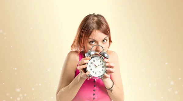 Vážné rusovláska dívka drží hodiny nad okr pozadí — Stock fotografie