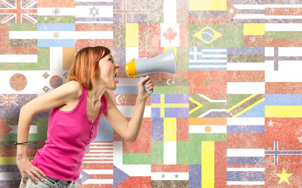 Rödhårig tjej skrika med en megafon över flaggor bakgrund — Stockfoto