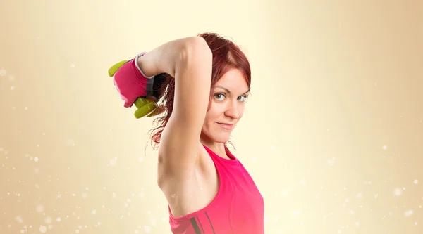 Redhead girl doing weightlifting over ocher background, — Stock Photo, Image