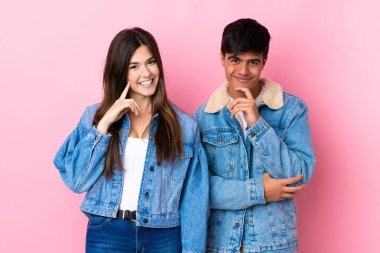 Soyutlanmış pembe arka planda tatlı bir ifadeyle gülümseyen genç çift.