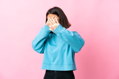 Pembe arka planda izole edilmiş genç Latin bir kadın gergin ellerini öne uzatıyor.