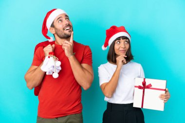 Noel şapkalı genç bir çift mavi arka planda izole edilmiş hediyeler dağıtıyor.