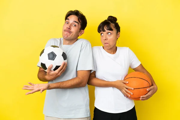 若いスポーツカップルがフットボールとバスケットボールを黄色の背景に孤立させて肩を持ち上げながら — ストック写真