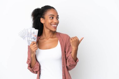 Genç Afrikalı Amerikalı bir kadın beyaz arka planda izole edilmiş bir sürü para alıyor. Bir ürünü sunmak için kenarı işaret ediyor.