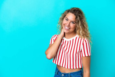 Kıvırcık saçlı kız mavi arka planda yalnız gülüyor.