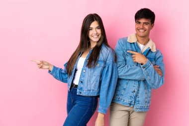 İzole edilmiş pembe arka plan üzerinde genç bir çift parmak yan pozisyonu işaret ediyor.