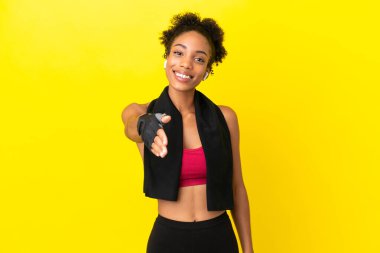 Sarı arka planda izole edilmiş genç Afrikalı spor kadını iyi bir anlaşma için el sıkışıyor.
