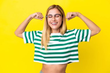 Sarışın Uruguaylı kız sarı arka planda izole edilmiş güçlü bir jest yapıyor.