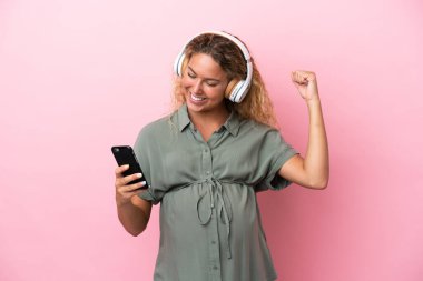 Kıvırcık saçlı kız pembe arka planda izole edilmiş hamile ve müzik dinlerken dans ediyor.