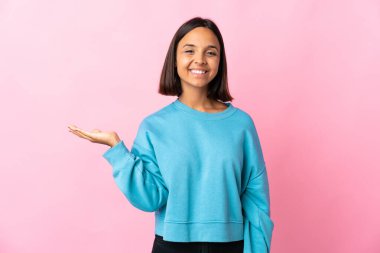 Pembe arka planda izole edilmiş genç Latin bir kadın bir ilan vermek için avucunun içinde hayali bir alan tutuyor.