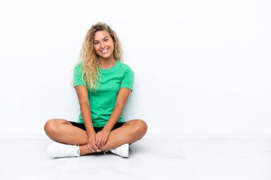 Kıvırcık saçlı kız yerde oturmuş gülüyor.