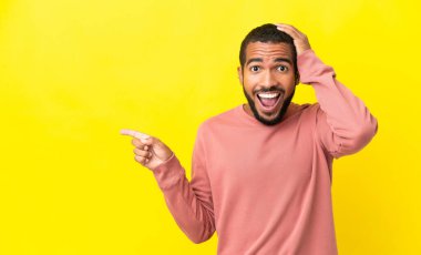 Sarı arka planda izole edilmiş genç latin adam şaşırdı ve parmağını yana çevirdi.