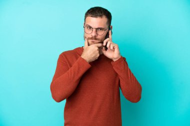 Mavi arka planda izole edilmiş cep telefonu kullanan genç Brezilyalı adam