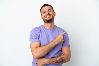 Beyaz arka planda izole edilmiş genç Brezilyalı bir adam bir ürün sunmak için kenarı işaret ediyor