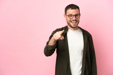 Pembe arka planda izole edilmiş genç Brezilyalı adam şaşırmış ve ön tarafı işaret ediyor.