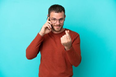 Mavi arka planda izole edilmiş cep telefonu kullanan genç Brezilyalı adam para hareketi yapıyor.