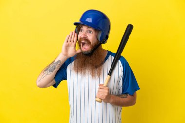 Kasklı ve yarasalı kızıl saçlı beyzbolcu sarı arka planda izole edilmiş ağzı açık bir şekilde bağırıyor.