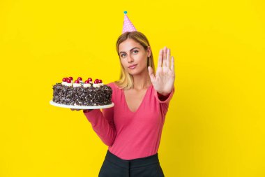 Sarışın Uruguaylı kız elinde doğum günü pastası tutuyordu. Sarı arka planda izole bir şekilde durup jest yapıyordu.
