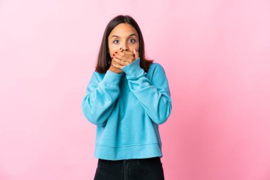 Pembe arka planda izole edilmiş genç Latin kadın ağzını kapatıyor ve yan tarafa bakıyor.