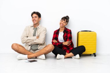 Genç melez ırk yolcuları, beyaz arka planda izole bir şekilde oturuyorlar. Kollarını yan yana koyup gülümsüyorlar.