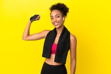 Sarı arka planda izole genç Afrikalı kadın güçlü bir jest yapıyor.