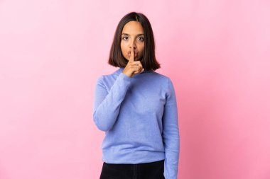 Pembe arka planda izole edilmiş genç Latin bir kadın sessizlik işareti gösteriyor. Parmağını ağzına sokuyor.