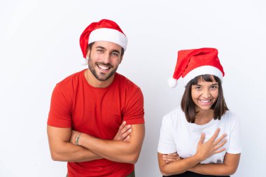 Beyaz arka planda izole edilmiş Noel şapkalı genç çift gülümserken kollarını çapraz tutuyorlar.