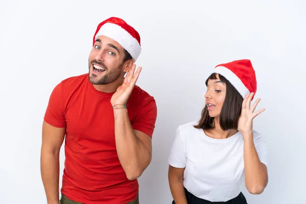 Junges Paar Mit Weihnachtsmütze Isoliert Auf Weißem Hintergrund Hört Etwas — Stockfoto