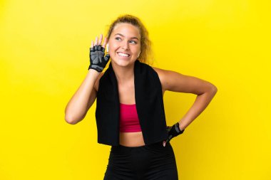 Sarı arka planda izole edilmiş havlusu olan sporcu kadın elini kulağına koyarak bir şeyler dinliyor.