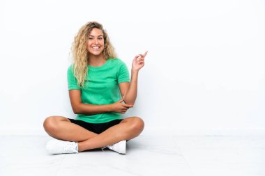 Kıvırcık saçlı kız yerde oturuyor ve parmağıyla işaret ediyor.