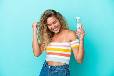 Mavi arka planda bir şişe suyu olan genç sarışın kadın zaferi kutluyor.