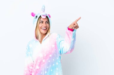 Sarışın Uruguaylı kız tek boynuzlu at pijaması giyiyor. Beyaz arka planda izole edilmiş. Parmakla göstererek bir ürün sunuyor.