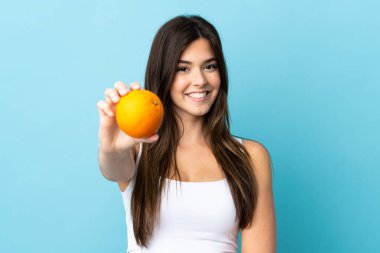 İzole edilmiş mavi arka planı olan Brezilyalı genç bir kız elinde portakal tutuyor.