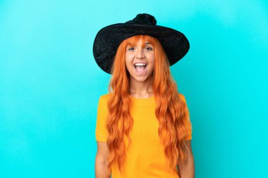 Cadı kılığına girmiş genç bir kadın. Mavi arka planda izole edilmiş ve yüzünde sürpriz bir ifade var.