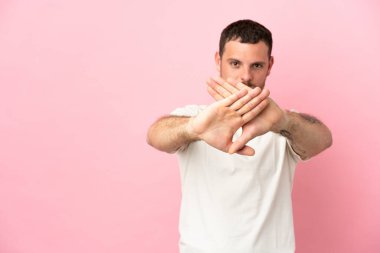 Pembe arka planda izole edilmiş genç Brezilyalı bir adam bir hareketi durdurmak için eliyle jest yapıyor.