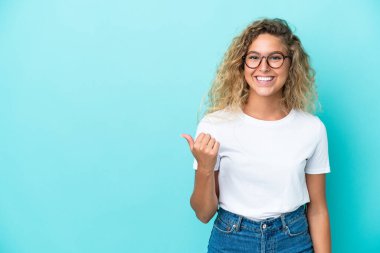 Mavi arka planda yalıtılmış kıvırcık saçlı kız bir ürünü sunmak için kenarı işaret ediyor.